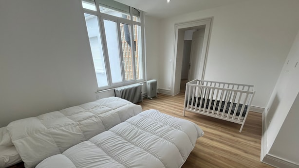 Quarto com duas camas, um berço, um radiador e uma janela.