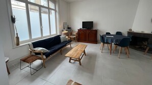 Uma sala de estar com sofá, mesa de centro de madeira, mesa de jantar com cadeiras, televisão e lareira.