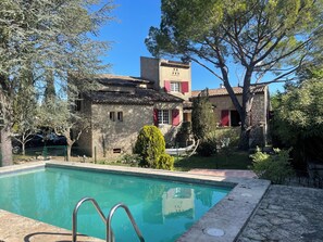 Un bâtiment en pierre doté d’une piscine, entouré d’arbres et d’une zone délimitée par une clôture.