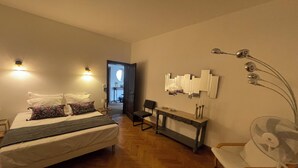 A hotel room with a bed, bedside table, chair, and a desk with a mirror and decorative items. - Villa en plein coeur d'Uzès (Uzès)