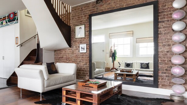 A modern living room with a white sofa, a wooden coffee table, a large mirror, and a brick wall. - Codrington Mews III by Onefinestay (London)