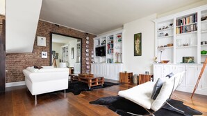 A modern living room with a white sofa, a black leather rug, and a brick wall. - Codrington Mews III by Onefinestay (London)