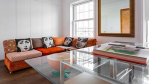 A modern living room with a glass coffee table, orange patterned sofa, and large windows. - Fulham Road X by Onefinestay (London)