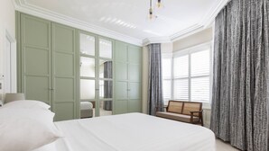 Een slaapkamer met een groot bed, een groene kast, een raam met gordijnen en een bankje bij het raam.