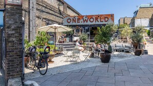 Een buitenruimte met tafels en stoelen, een fiets en een bord waarop 'ONE WORLD' staat.