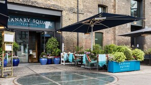 An outdoor seating area with tables and chairs, a blue planter with 'GRANARY SQUARE BRASSERIE' text, and a glass door entrance to the establishment. - Keystone Crescent by Onefinestay (London)