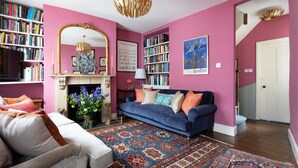 A living room with a blue sofa, a white armchair, a fireplace, and a bookshelf filled with books. - Keystone Crescent by Onefinestay (London)