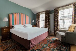 A hotel room with a large bed, a chair, a dresser, and a window with curtains. - Keystone Crescent by Onefinestay (London)
