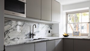 Een keuken met een marmeren aanrechtblad, een ingebouwde magnetron en grijze keukenkastjes.