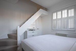 A bedroom with a bed, a white dresser, a white radiator, and a window with shutters.