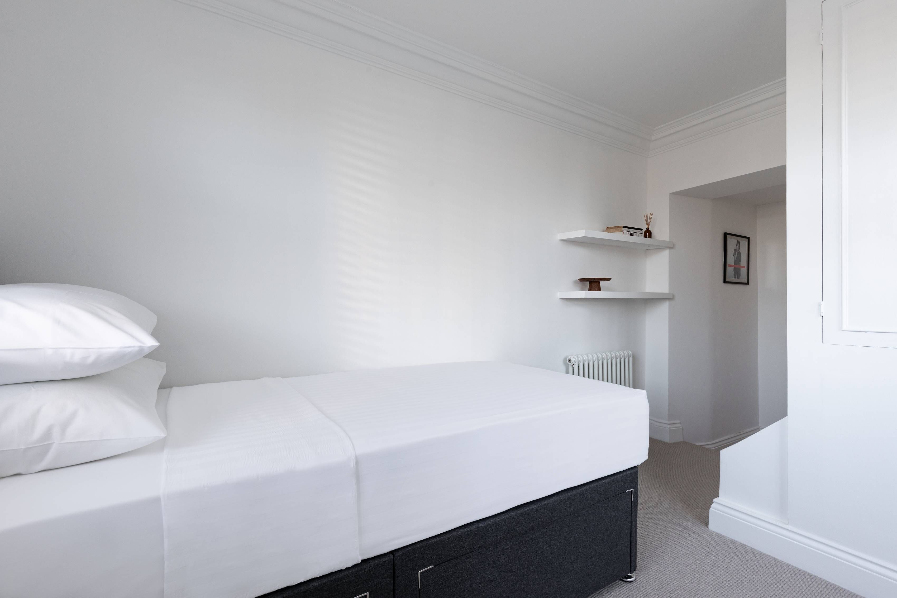 Un dormitorio minimalista con cama, paredes blancas y un radiador.