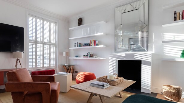 A modern living room with a sofa, a coffee table, and a TV. There are bookshelves and a fireplace. - St Stephen's Gardens VII by Onefinestay (London)