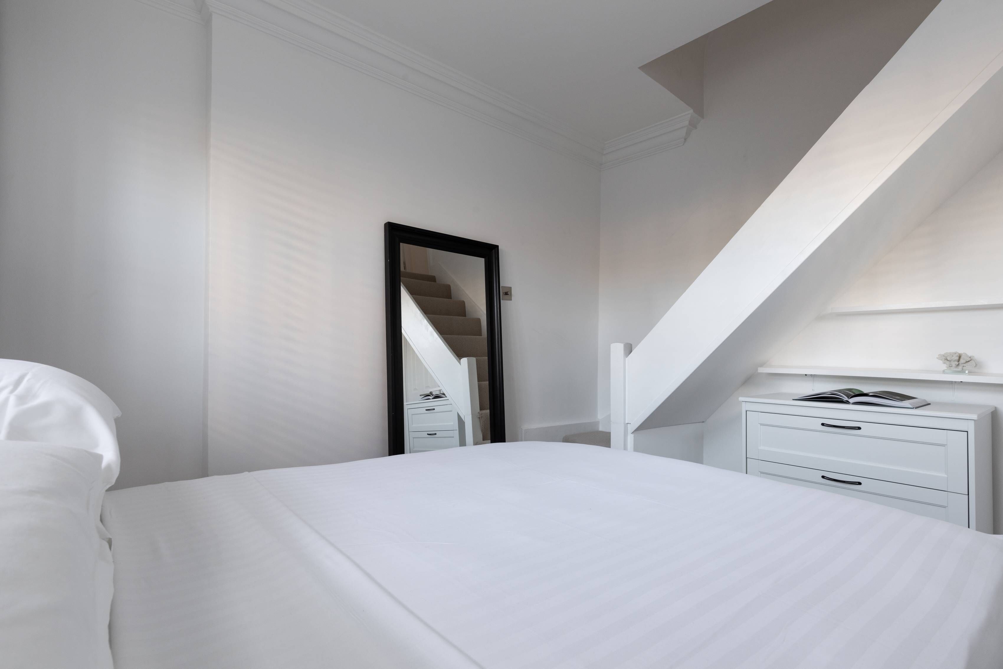 Un dormitorio con una cama grande, una mesita de noche, un espejo y una escalera que conduce a un nivel superior.