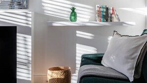 A modern living room with a green sofa, white shelves with books and decorative items, a woven basket, and a mirror with a geometric design. - St Stephen's Gardens VII by Onefinestay (London)