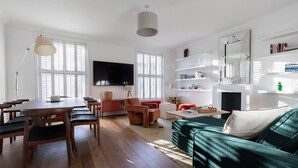 A modern living room with a wooden dining table, chairs, a sofa, and a TV. - St Stephen's Gardens VII by Onefinestay (London)