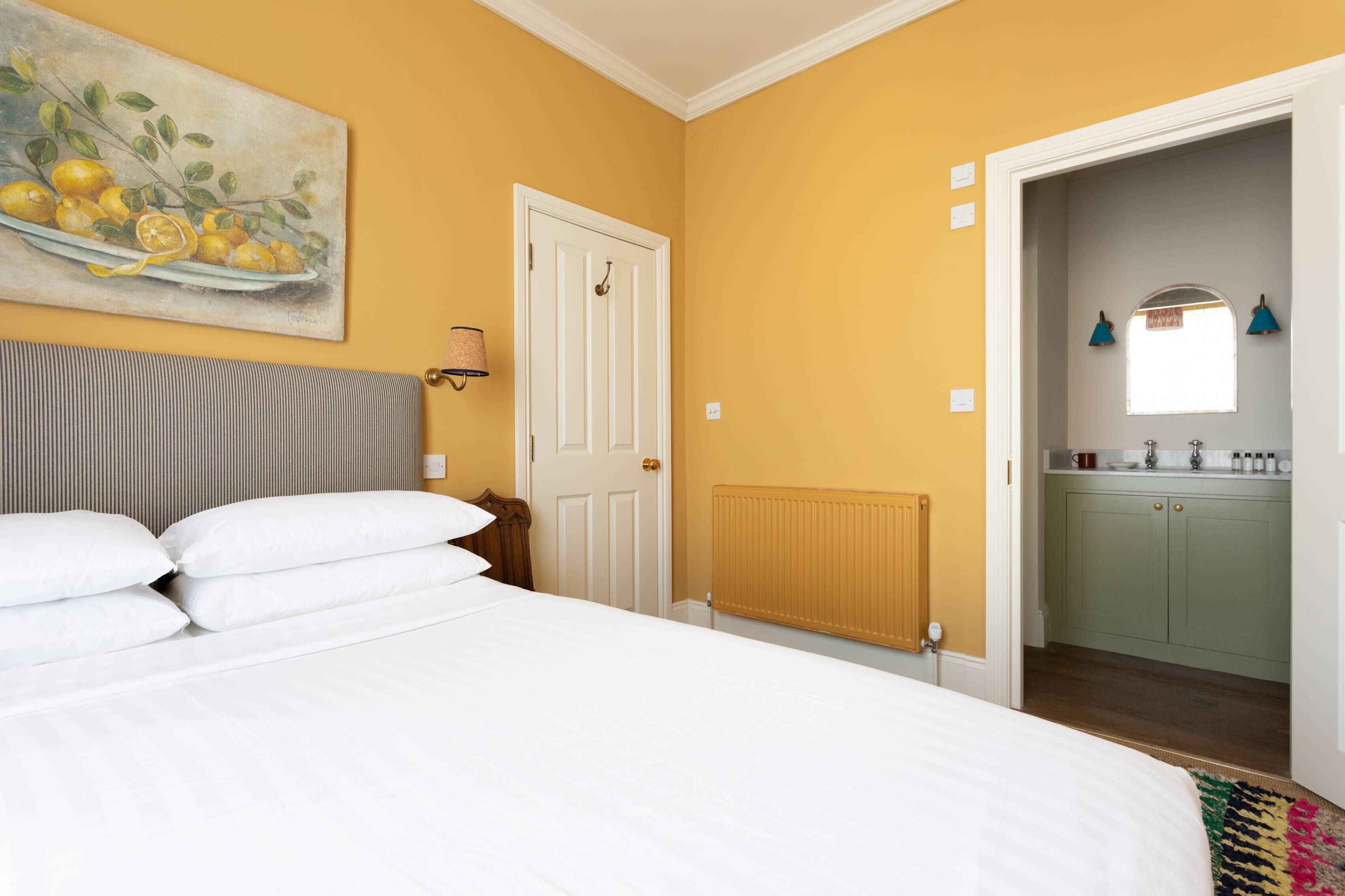 Een slaapkamer met een bed, een witte deur, een radiator en uitzicht op een keuken.