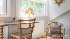 Een kamer met een houten bureau, twee rieten stoelen, een zacht tapijt en een zonachtige decoratie aan de muur.