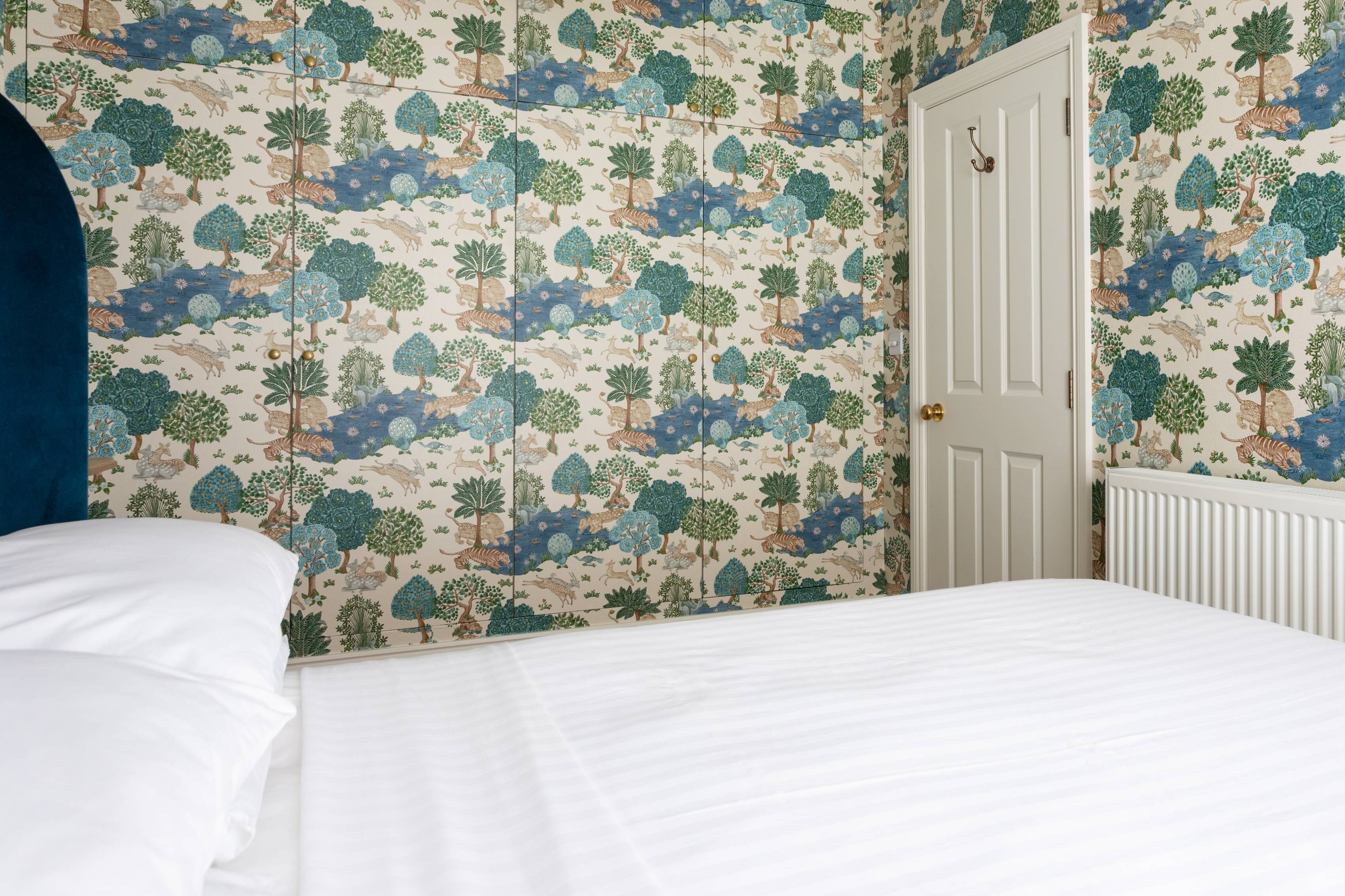 A bedroom with a bed, white bedding, and a wall with a nature-themed wallpaper.