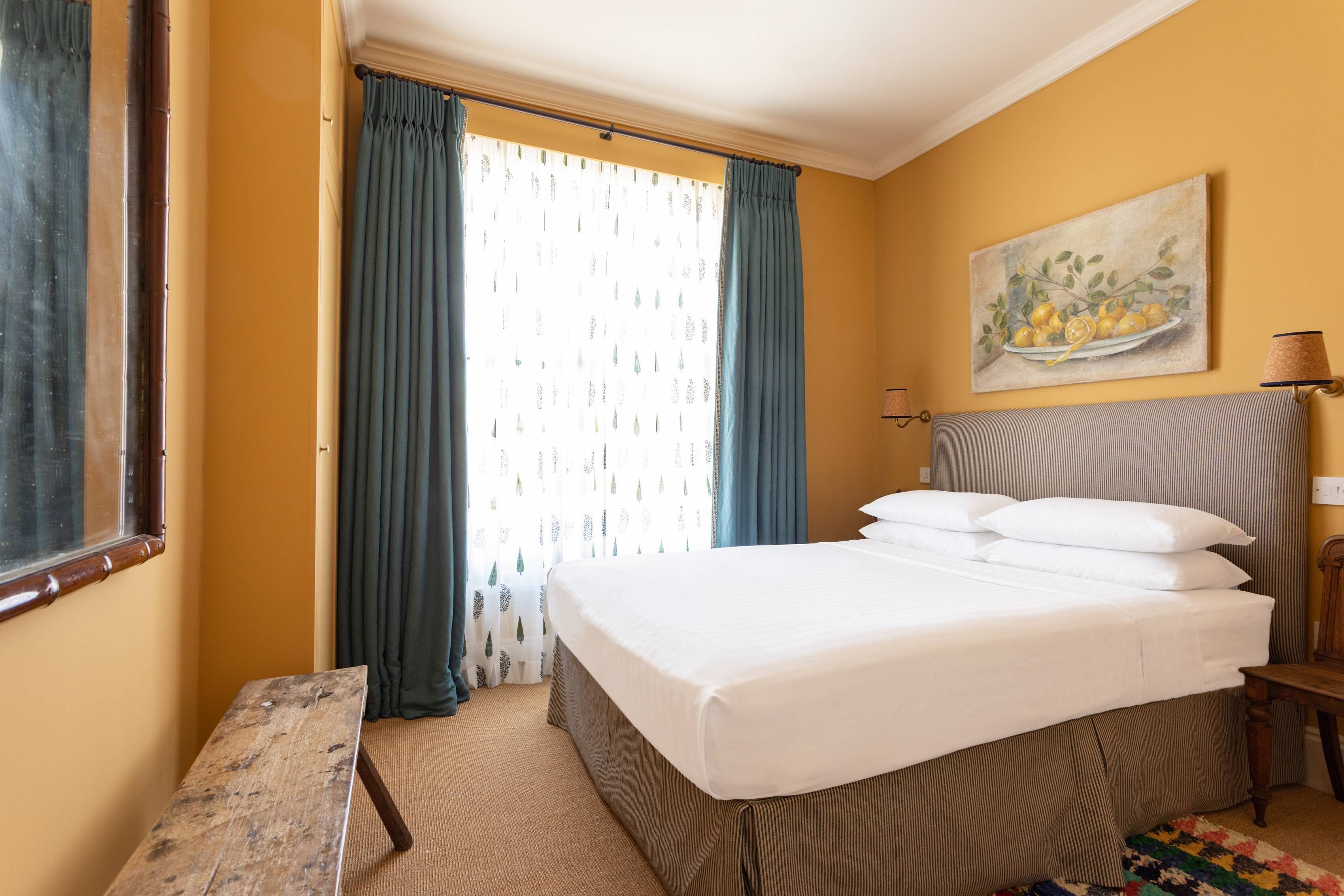 A hotel room with a bed, a desk, a lamp, and a painting on the wall.