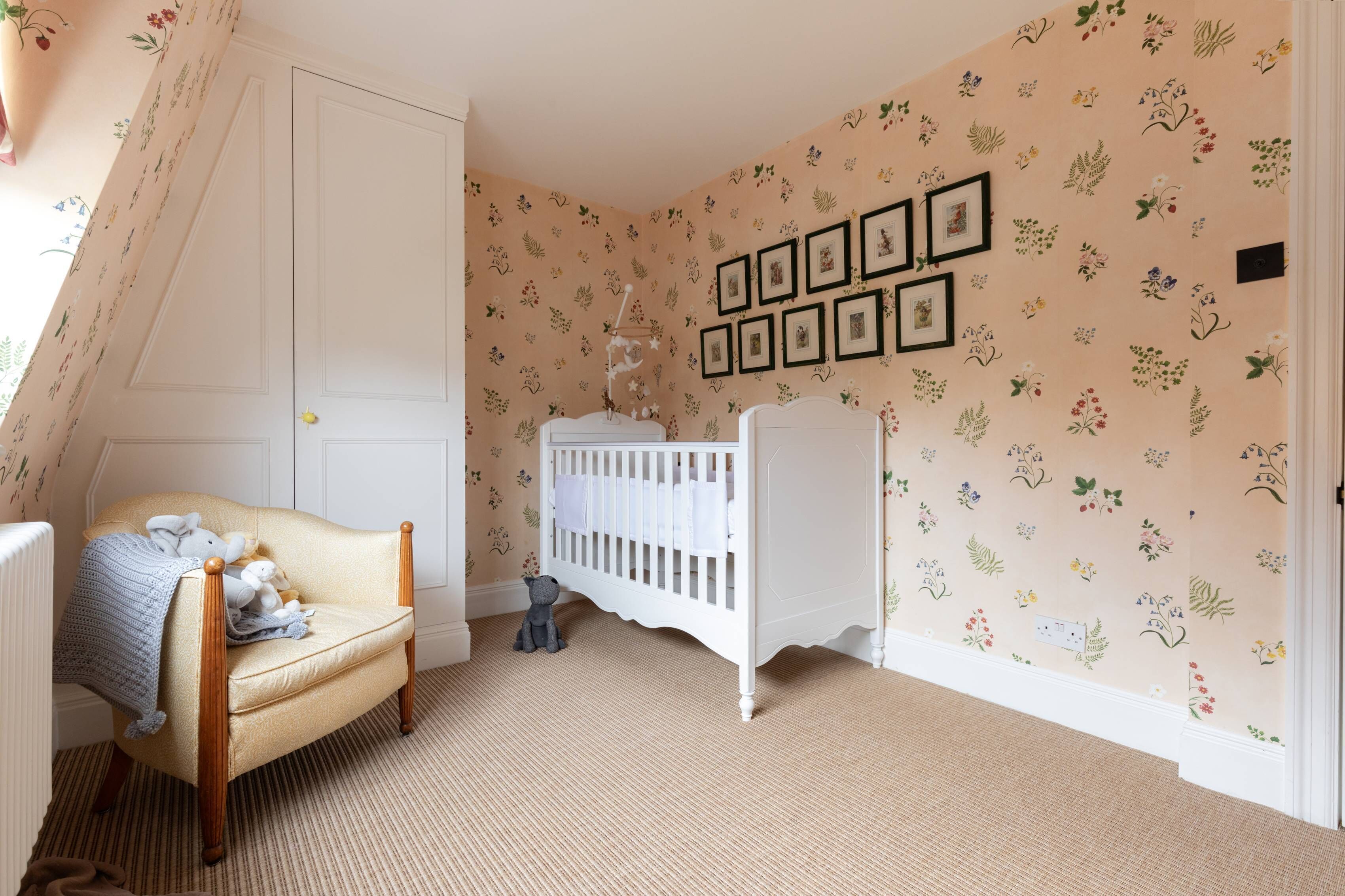 A cozy room with a crib, a chair with toys, and a wall with framed pictures.