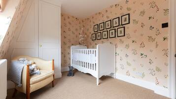 A cozy room with a crib, a chair with toys, and a wall with framed pictures.