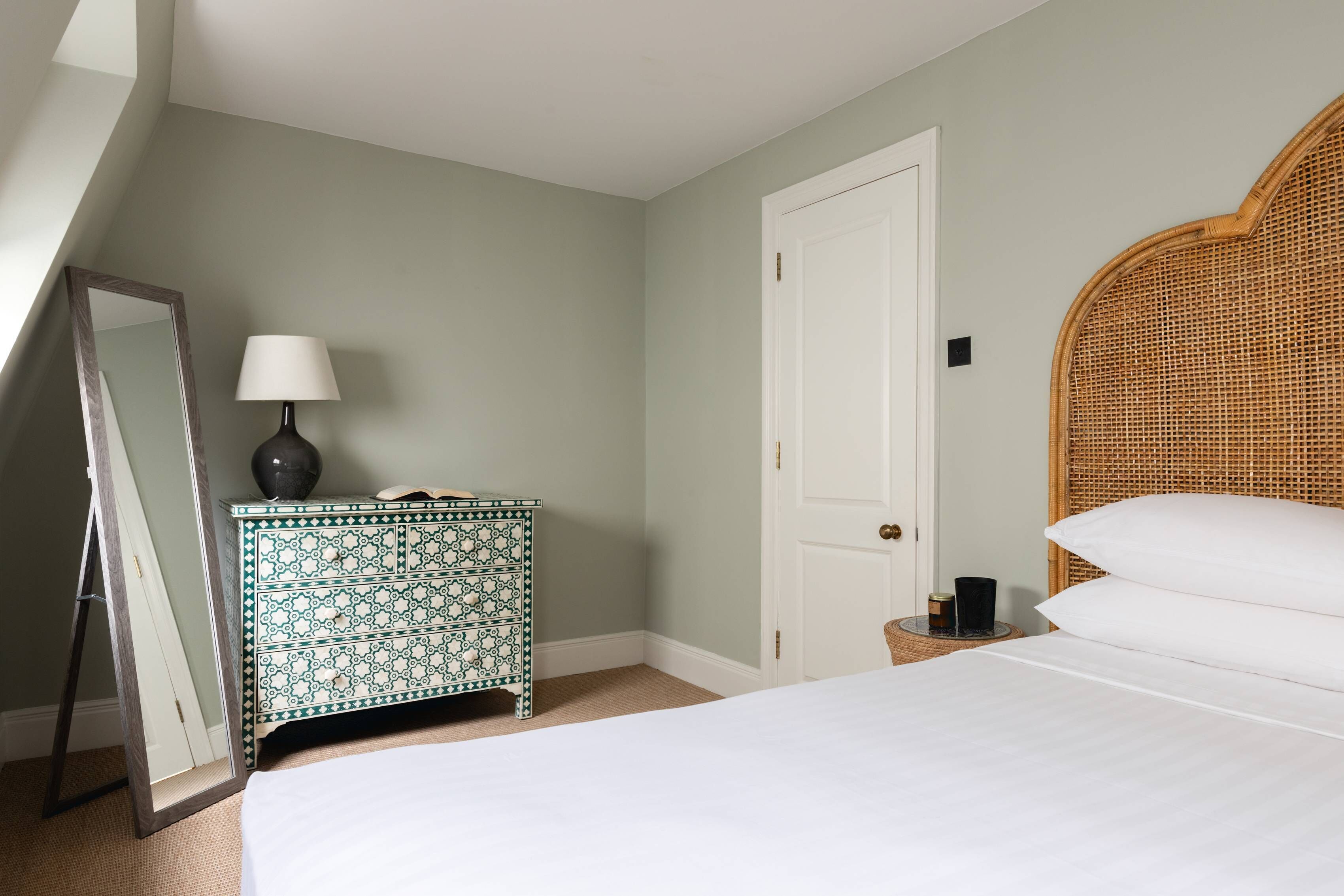 A bedroom with a bed, a dresser, a mirror, a lamp, and a door.