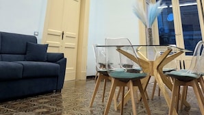 A room with a dark blue sofa, a glass table with chairs, and a decorative ceiling with floral patterns. - Trewhella Home, centro storico, Duomo (Catania)