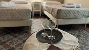 A hotel room with two beds, a small table with two wine glasses, and a nightstand with a lamp. - Trewhella Home, centro storico, Duomo (Catania)