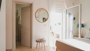 A bedroom with a large mirror, a bedside table with a lamp, and a view of the bathroom. - fraledune (Maruggio)