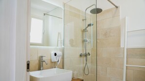 A modern bathroom with a glass-enclosed shower, a white sink, and a handheld hair dryer on the counter. - fraledune (Maruggio)