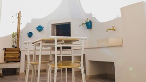 An outdoor patio with a table and chairs under a large umbrella, a sink, and decorative blue pots on the wall. - fraledune (Maruggio)