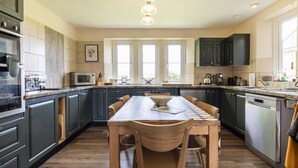 A modern kitchen with dark cabinets, a central island, and a dining area. - Gorgeous Rural 4 Bed Farm Cottage - With Hot Tub (Norton Saint Philip)
