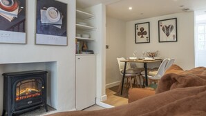 A cozy living room with a fireplace, a dining area with a table and chairs, and artwork on the walls. - Cosy 2BD Cottage in Oxfordshire - Near Daylesford (Kingham)
