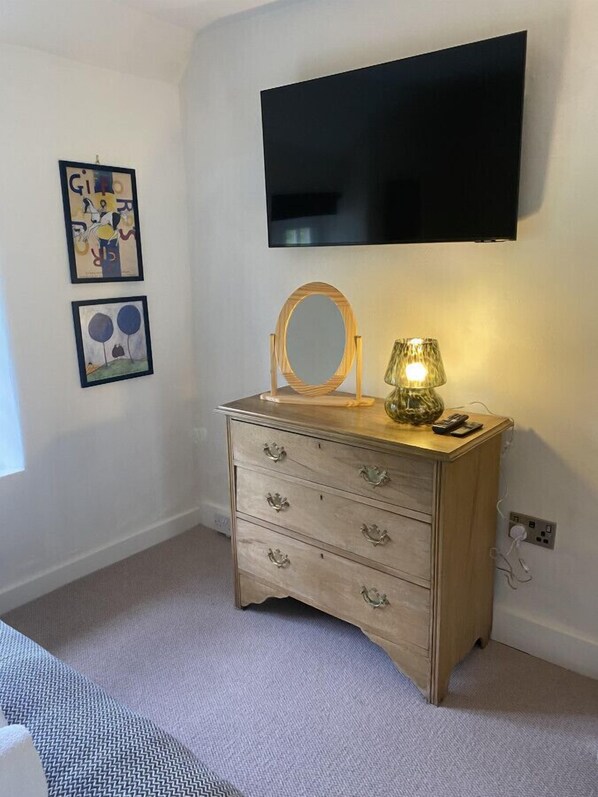 A bedroom with a wooden dresser, a TV mounted on the wall, and two framed artworks on the wall. - Cosy 2BD Cottage in Oxfordshire - Near Daylesford (Kingham)