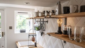 A kitchen with wooden shelves, hanging utensils, and a light bulb. - Cosy 2BD Cottage in Oxfordshire - Near Daylesford (Kingham)