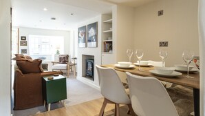 A modern dining area with a wooden table set for four, white chairs, and a fireplace. - Cosy 2BD Cottage in Oxfordshire - Near Daylesford (Kingham)