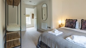 A bedroom with a bed, a large mirror, a wooden shelf, and a radiator. - Cosy 2BD Cottage in Oxfordshire - Near Daylesford (Kingham)