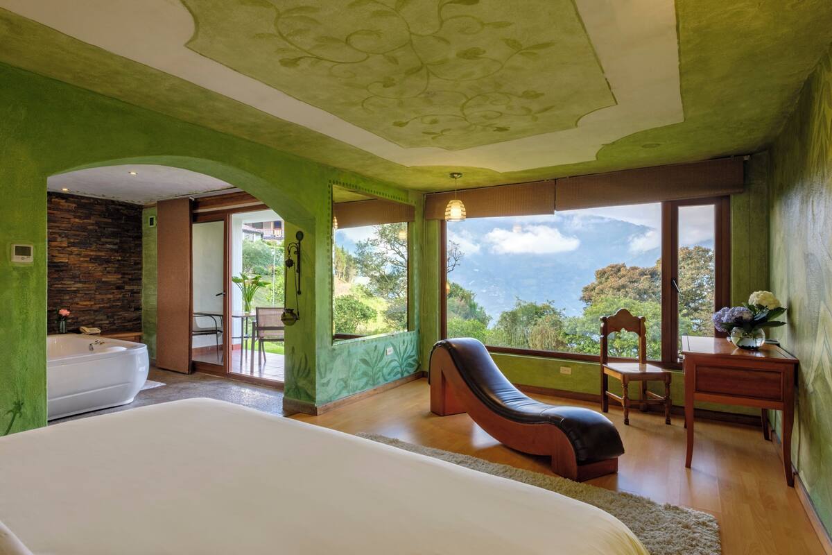 A bedroom with a large bed, a massage chair, a wooden desk, and a view of the outdoors.