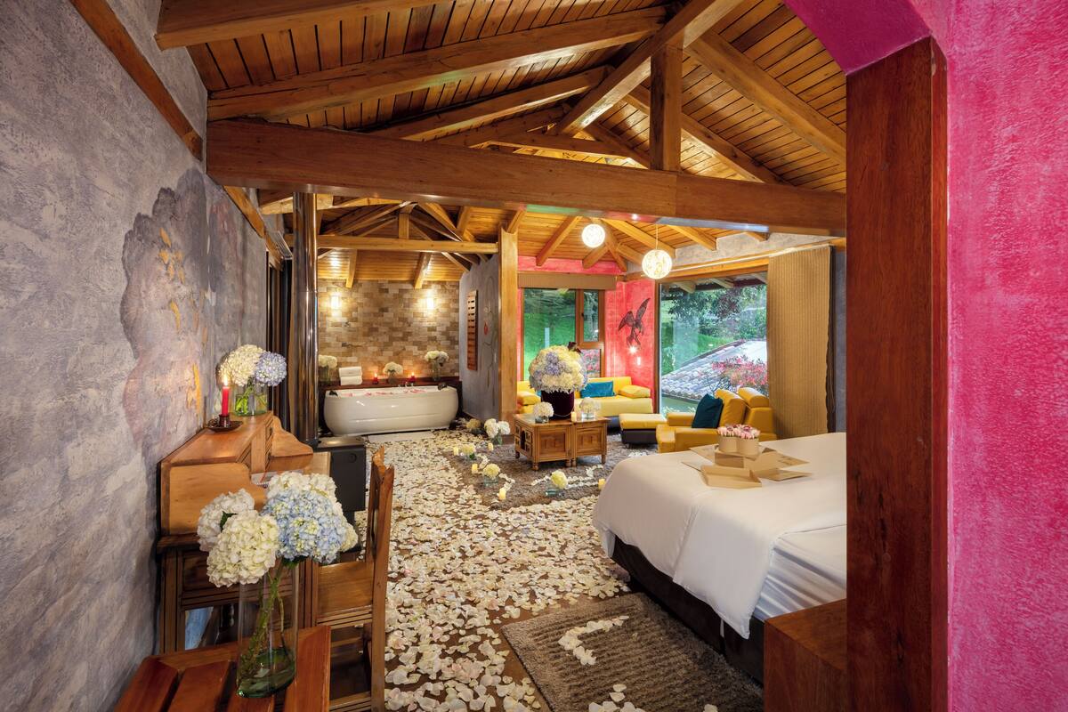 A room with a wooden ceiling, a large bed, a bathtub, and a sofa.