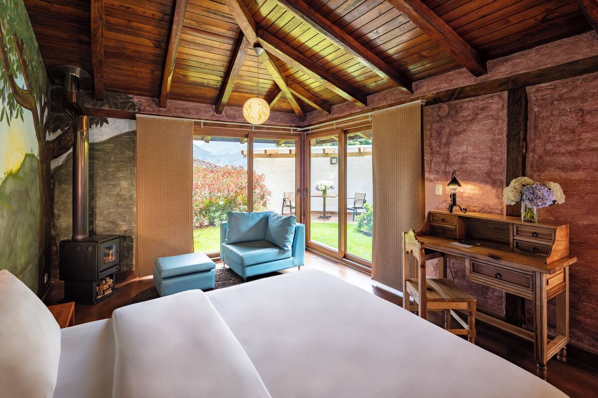A bedroom with a large bed, a blue armchair, a wooden desk, and a fireplace.