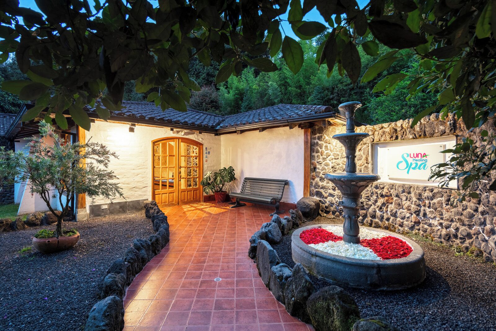 A spa entrance with a stone wall, a wooden door, a bench, and a fountain.