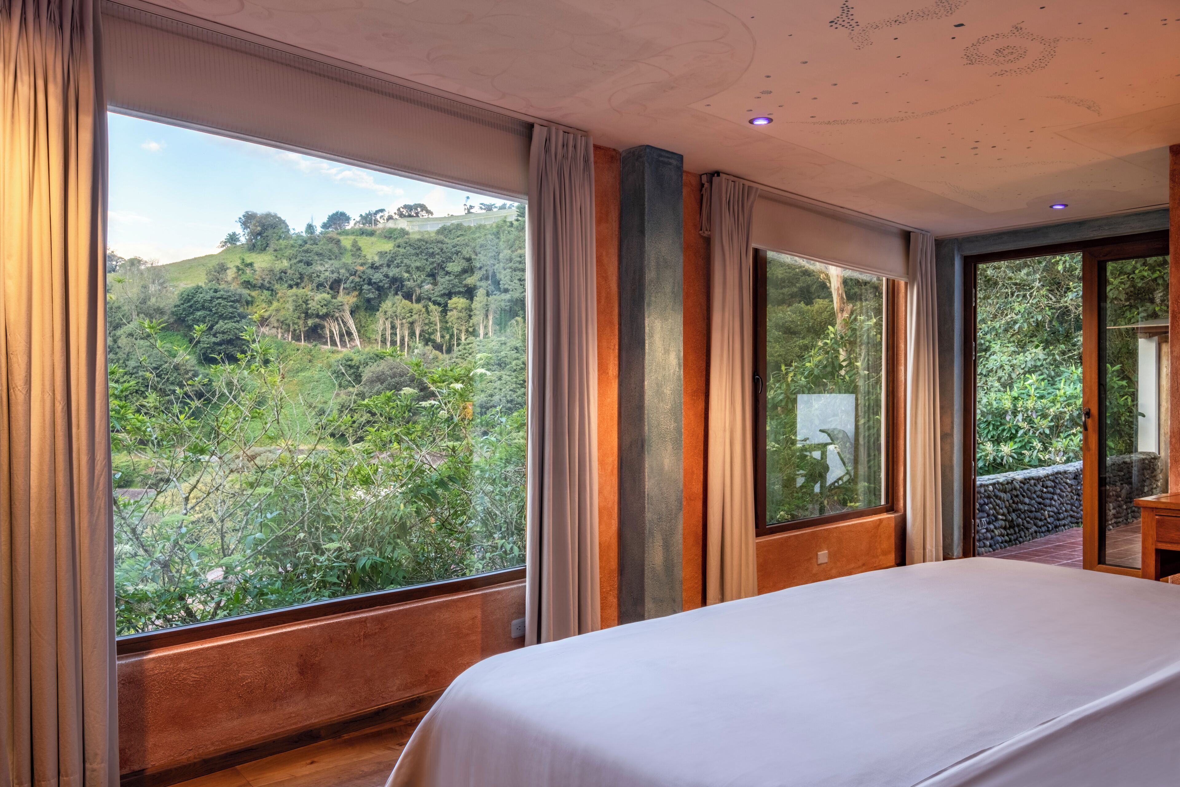 A bedroom with large windows offering a view of a lush, green landscape.