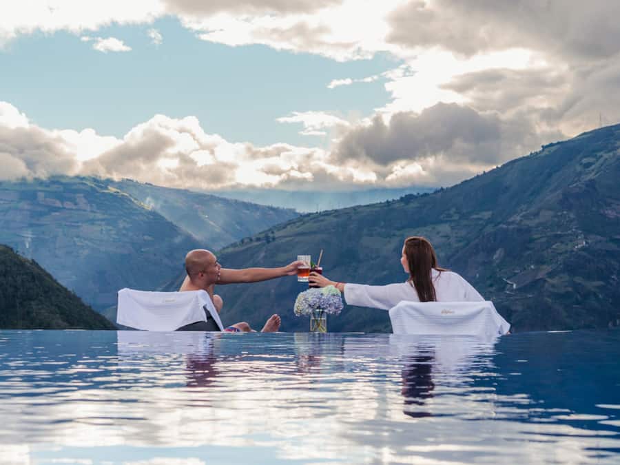 Una pareja en una piscina azul cristalina, con un paisaje montañoso al fondo.