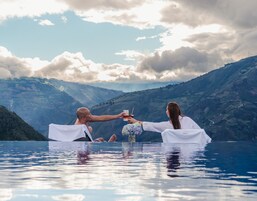 Una pareja en una piscina azul cristalina, con un paisaje montañoso al fondo.