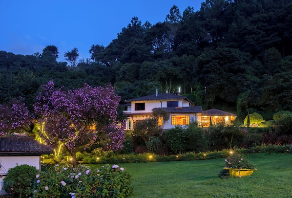 Ein Haus, umgeben von üppigem Grün und blühenden Pflanzen, mit einem gepflegten Garten und freiem Blick auf den umliegenden Wald.