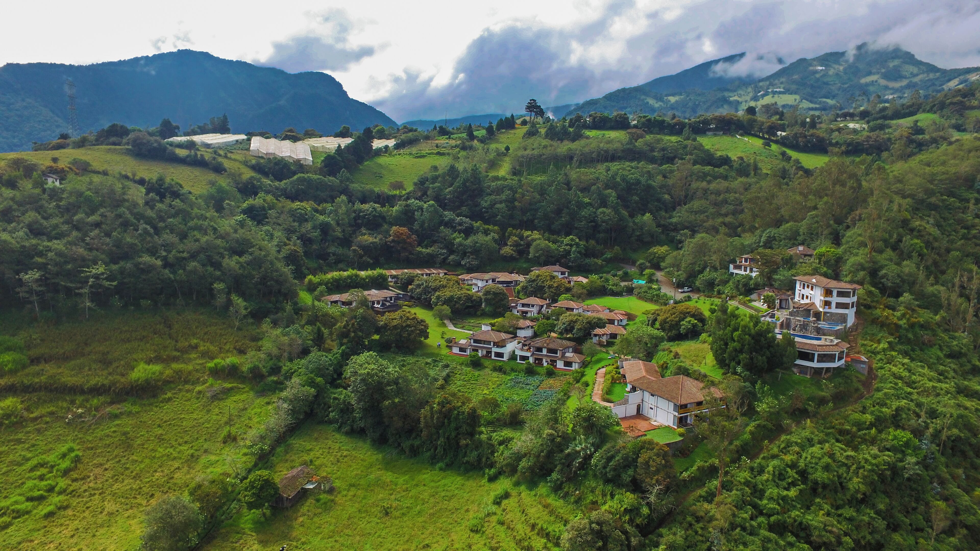 A hilly village with traditional houses surrounded by lush greenery and mountains in the background.