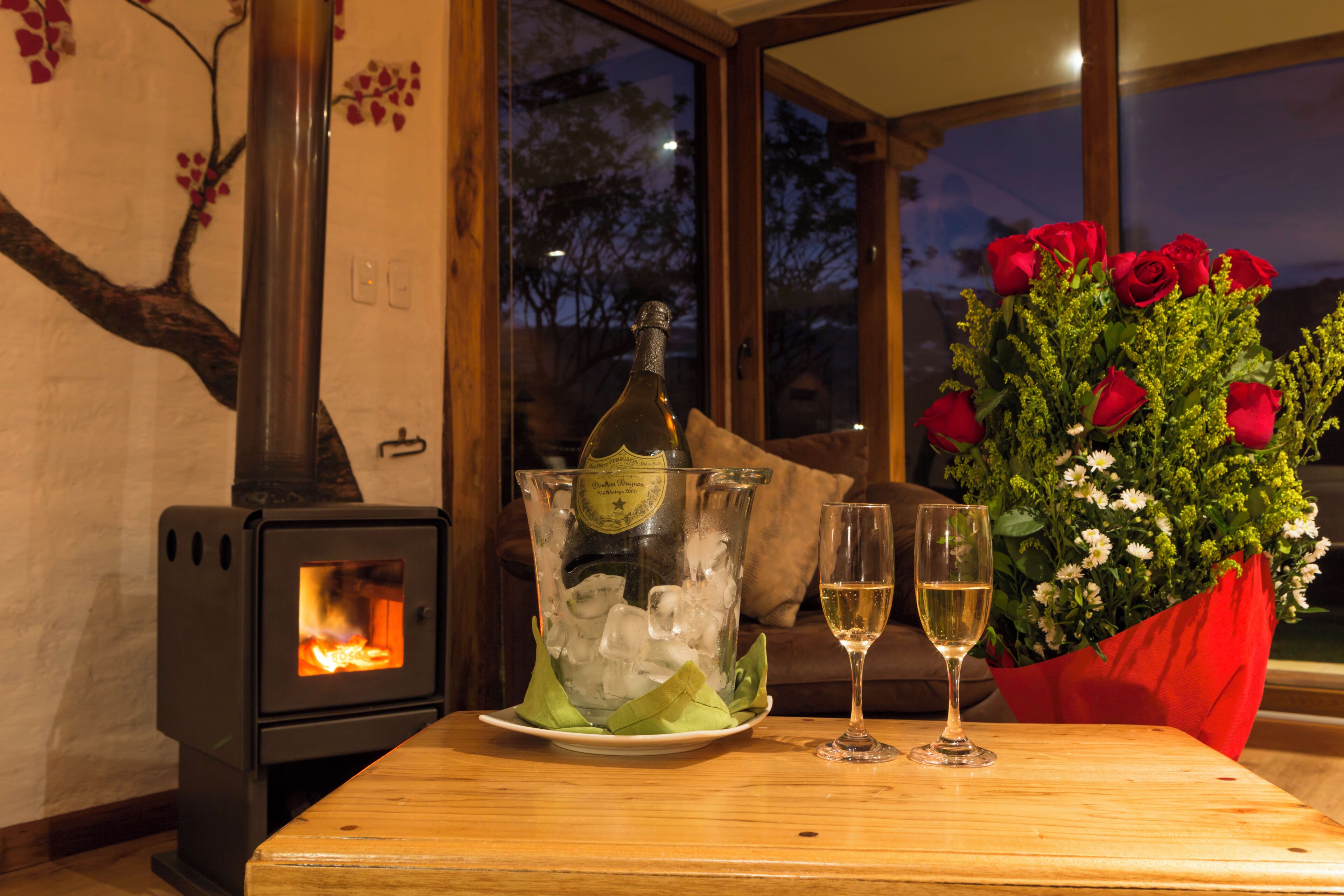 Een gezellige kamer met een houtkachel, een tafel met champagne, twee glazen en een boeket rode rozen.