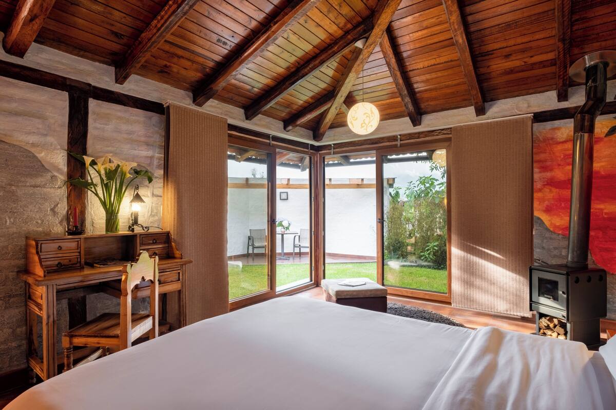 A bedroom with a large bed, wooden desk, and a fireplace.