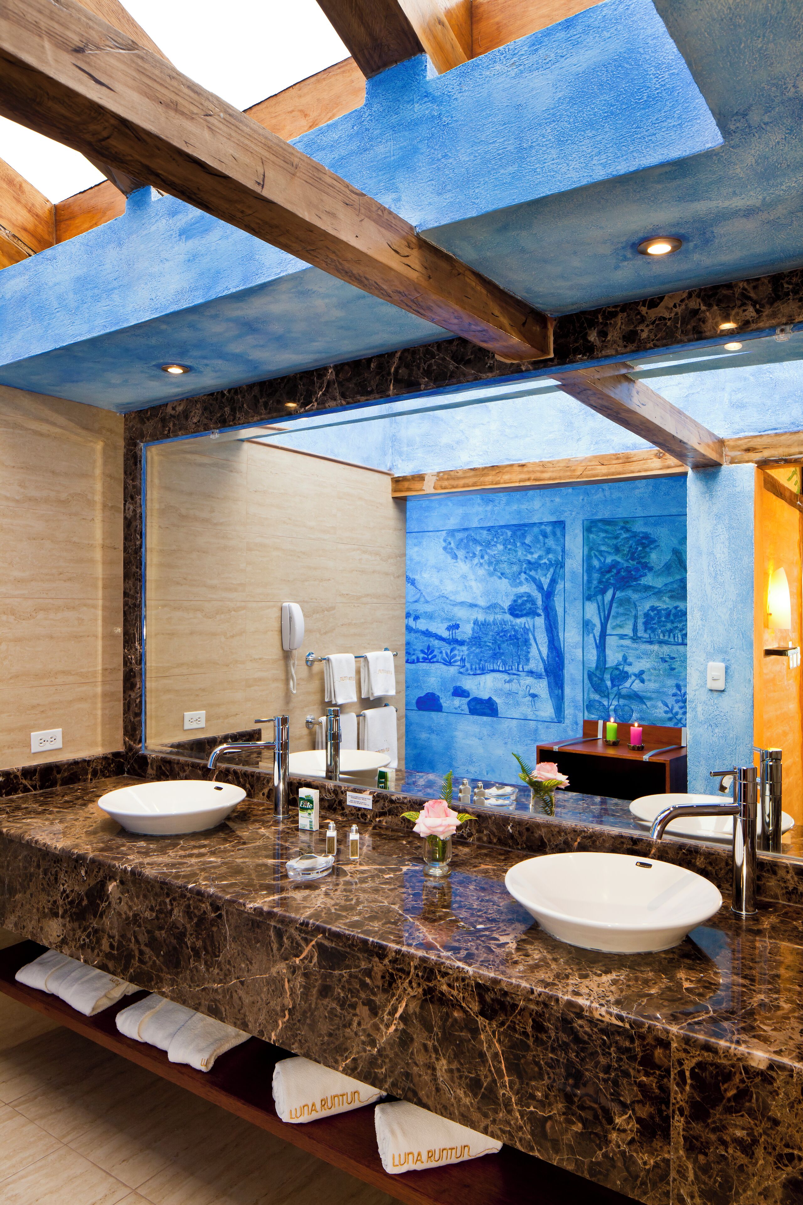 Un baño moderno con dos lavabos, encimeras de mármol, un tragaluz y un mural en la pared.