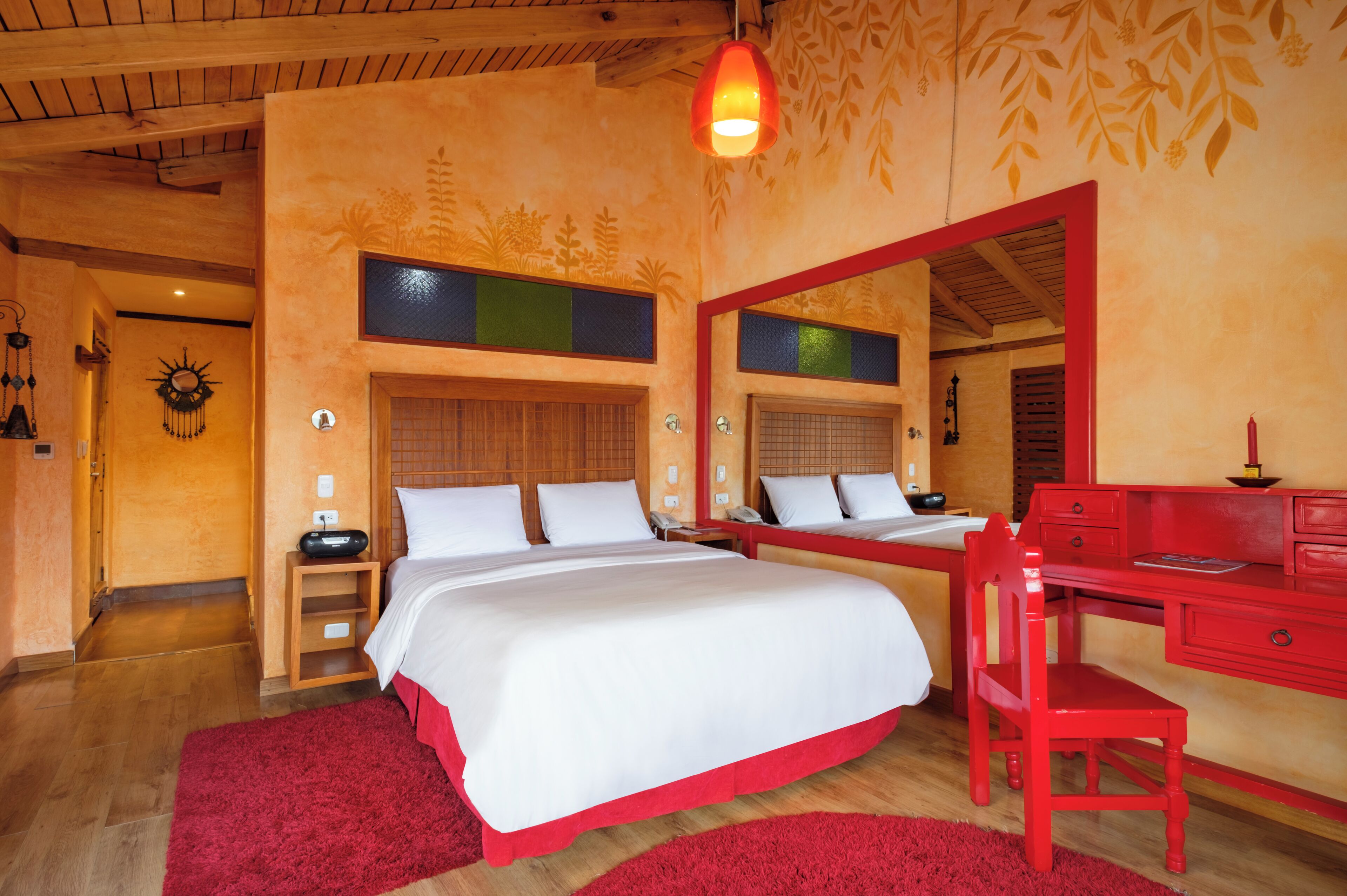 A bedroom with a large bed, a red desk, and a mirror.